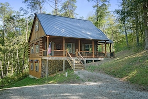 Eine rustikale Holzhütte mit Steinfundament, Holzfassade und einem Metall-Dach. Sie hat eine Veranda mit einer Treppe, die zu einer Terrasse führt.