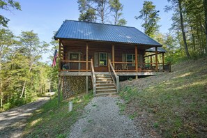 Une cabane en rondins avec un toit en métal, une terrasse en bois et des fondations en pierres.