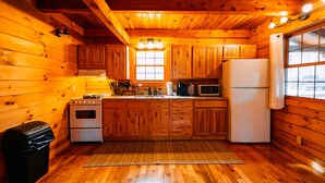 L’intérieur d’un chalet en bois comprend une cuisine équipée de meubles en bois, d’une cuisinière, d’un réfrigérateur et d’une fenêtre.