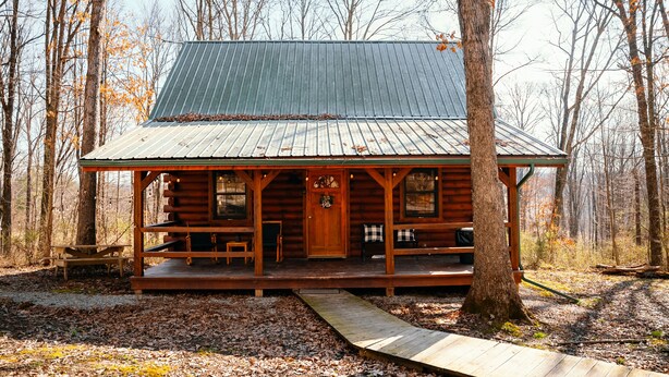 Une cabane en rondins dotée d’un porche, d’une terrasse en bois et d’un toit en métal.