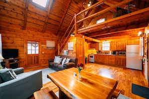 A log cabin interior with a dining area, kitchen, and living room.