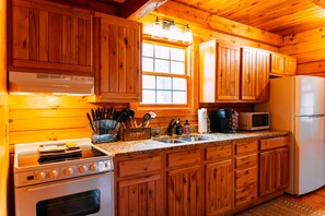 Interior de una cabaña de madera con cocina equipada con estufa, horno, microondas, pileta y armarios de madera.