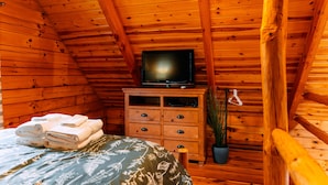 Une chambre dans un chalet en bois, avec un lit, une commode, un téléviseur et une plante en pot.