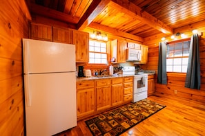 Una cocina estilo cabaña de madera con armarios de madera, un refrigerador, una estufa y una ventana con cortinas.