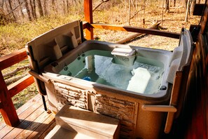 A hot tub with a stone exterior, wooden deck, and a wooden railing.