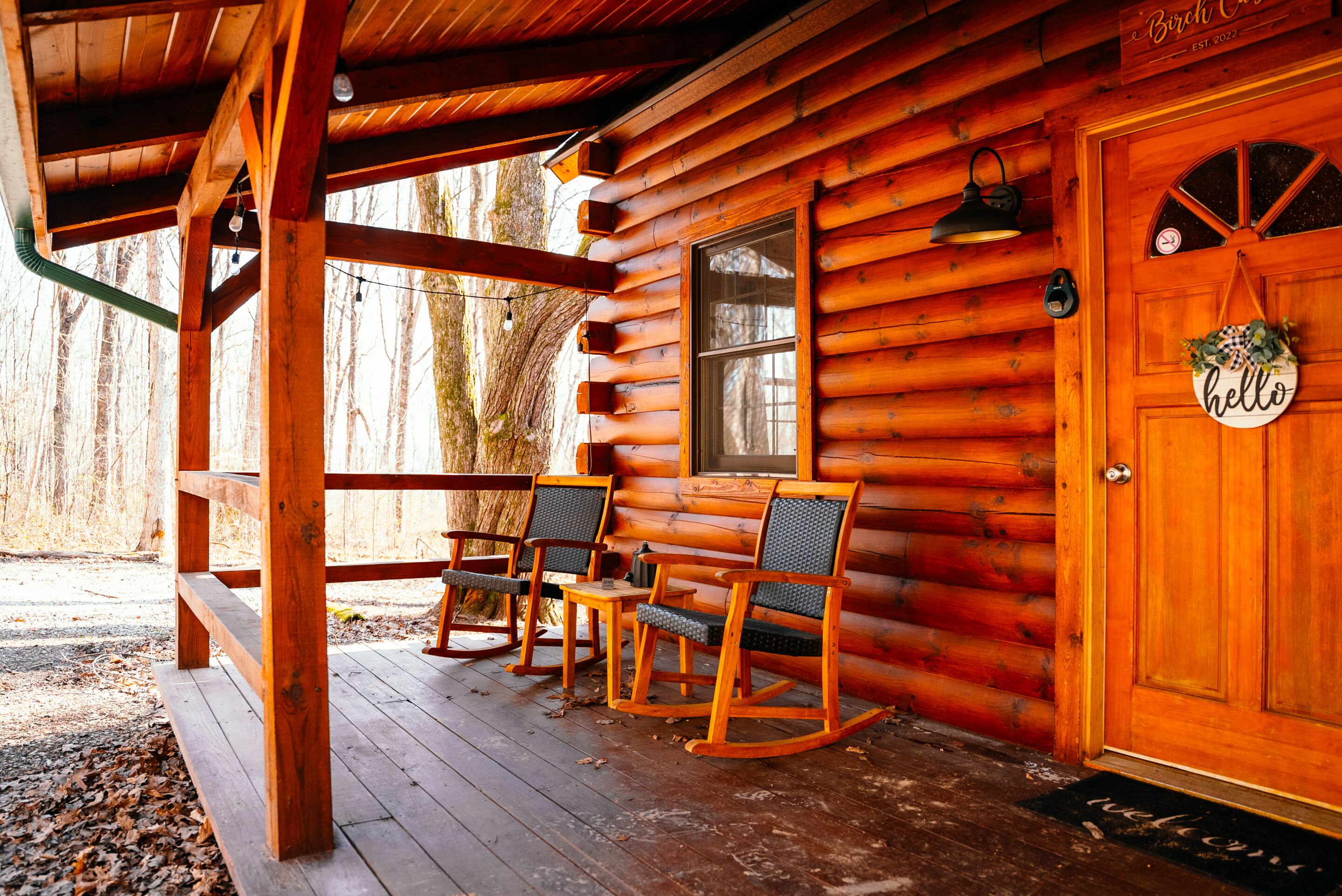 Eine Blockhütte mit Veranda, Schaukelstühlen, einer Holztür mit einem 'hello'-Schild und einem Fenster.