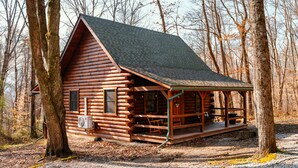 Une cabane en rondins avec un porche et une cheminée, entourée d’arbres.