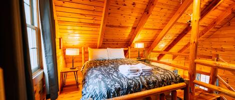 Une chambre dans une cabane en bois, avec un lit, deux lampes de chevet et une fenêtre.