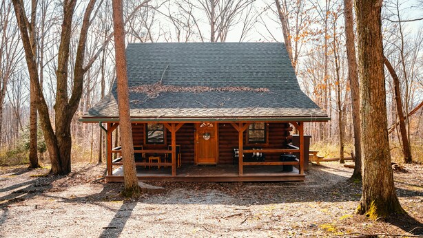 Une cabane en rondins avec une véranda, une porte d’entrée et un banc à l’extérieur.