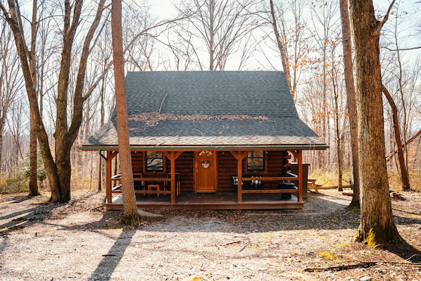 A log cabin with a porch, a front door, and a bench outside.