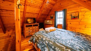 Een slaapkamer in een houten hutje, met een bed, een kaptafel en een raam met gordijnen.
