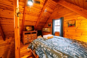 Een slaapkamer in een houten hutje, met een bed, een kaptafel en een raam met gordijnen.