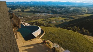 A pool with a curved edge, a stone deck, and a view of a valley with mountains in the background.