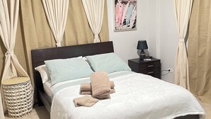 Ein ordentlich bezogenes Bett mit weißer Decke, einer Nachttischlampe und einem kleinen Nachttisch mit Lampe.