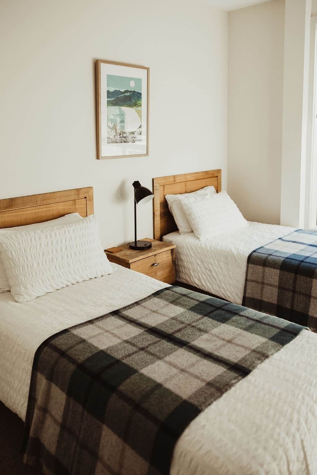 A hotel room with two beds, each with a wooden headboard, a nightstand with a lamp, and a framed picture on the wall.