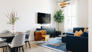 A modern living room with a round dining table, a sofa, a TV, and a large plant. - The Nook at The Purple Martin is a two bedroom one bath unit in Norton Commons (Prospect)