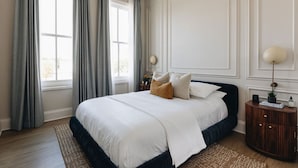 A bedroom with a large bed, grey curtains, a wooden nightstand, and a wall-mounted lamp. - The Nook at The Purple Martin is a two bedroom one bath unit in Norton Commons (Prospect)