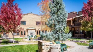 A courtyard with a stone planter, outdoor seating, and a building with a stone facade and multiple windows. - Condo at Bison Ranch with Resort Amenities (Overgaard)