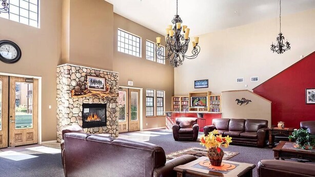 A spacious living room with a stone fireplace, leather sofas, a chandelier, and a red accent wall. - Condo at Bison Ranch with Resort Amenities (Overgaard)