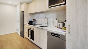 A modern kitchen with light wood cabinetry, stainless steel appliances, and a marble backsplash.