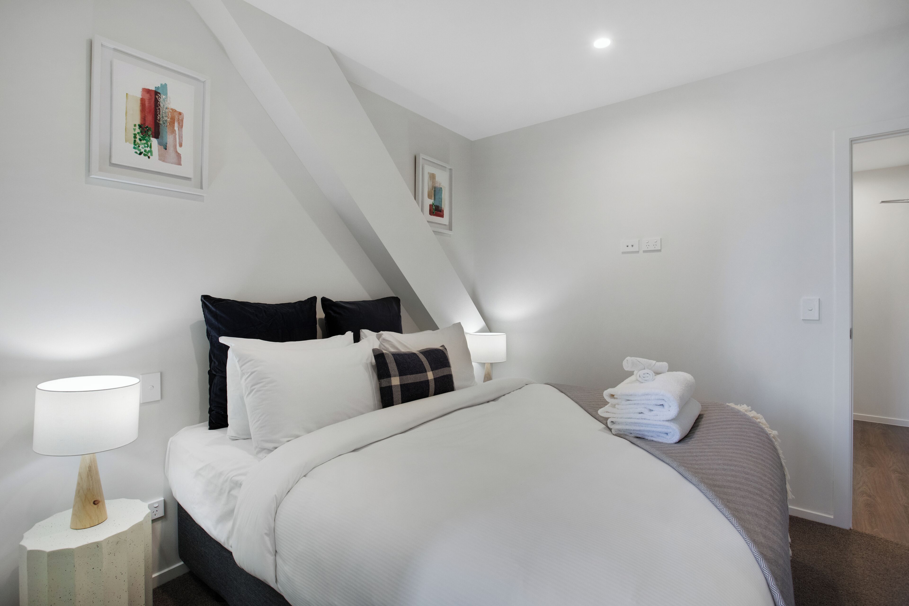 A neatly made bed with white bedding, a bedside lamp, and a folded towel on the side.