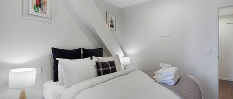 A neatly made bed with white bedding, a bedside lamp, and a folded towel on the side.