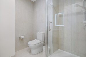 Moderni kylpyhuone, jossa on wc, lasinen suihkuseinä ja wc-paperiteline.