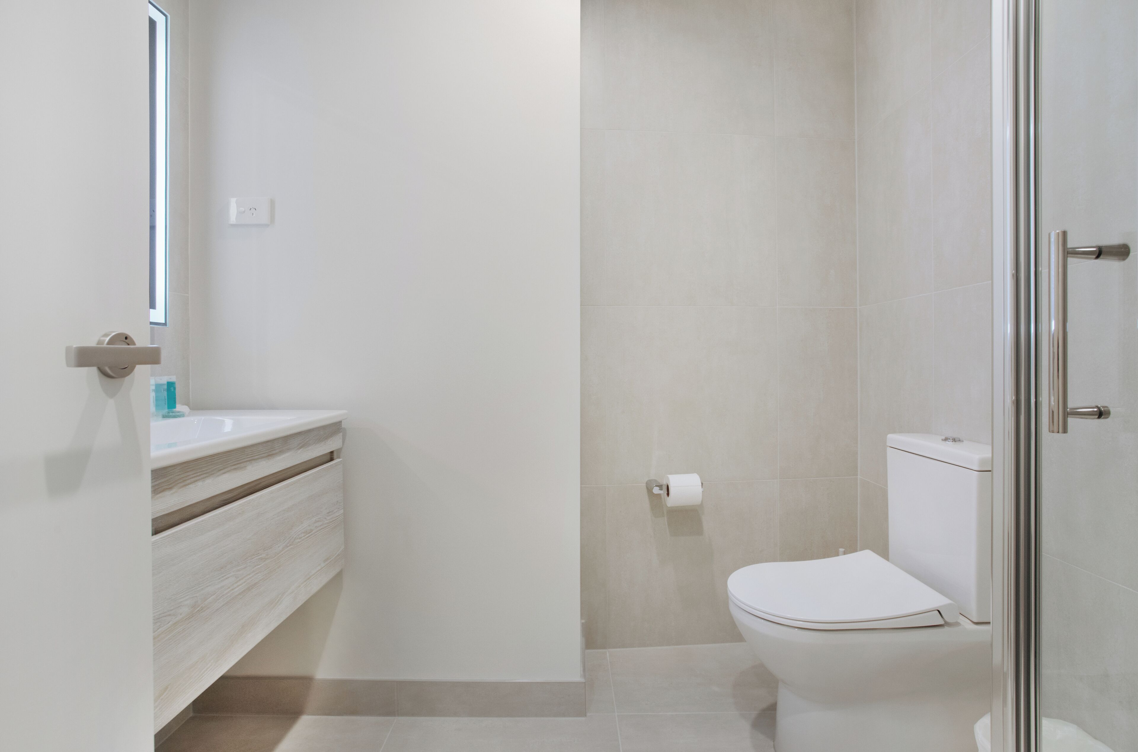 Une salle de bain moderne avec une douche à l’italienne en verre, des toilettes blanches et un meuble-lavabo avec un miroir.
