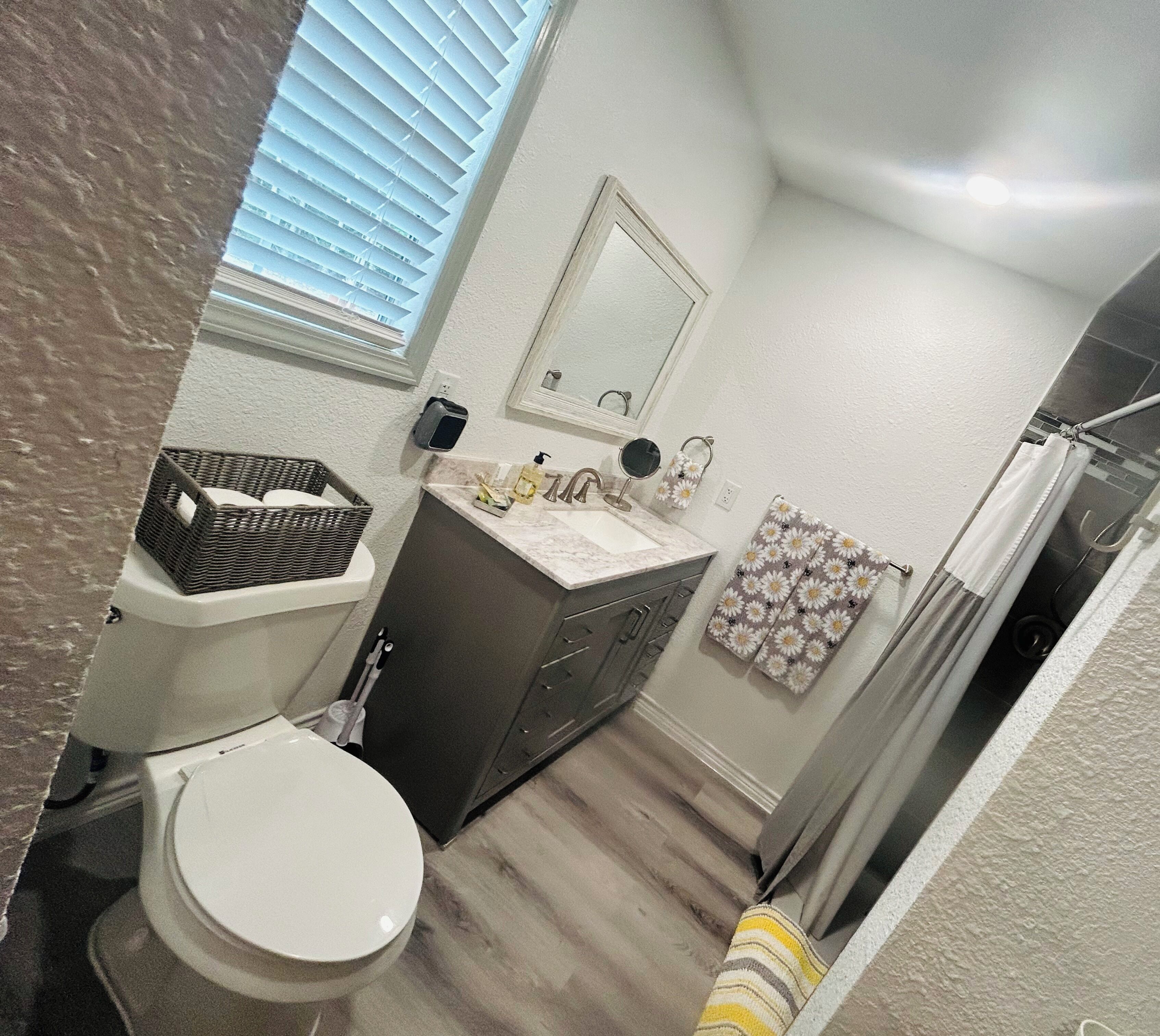A compact bathroom with a toilet, sink, and mirror. There is a basket on the floor and a towel rack with a floral towel.