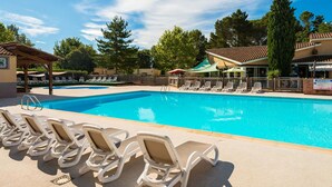 En swimmingpool med liggestole, et overdækket loungeområde og en bygning med teksten "PISCINE".