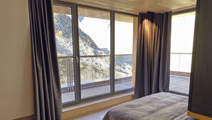 Ein Schlafzimmer mit großem Fenster und Blick auf die Berge, Holzboden und Bett mit Decke.