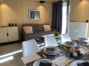 Una sala moderna con un sofá gris, sillas blancas y una mesa de comedor lista para una comida.