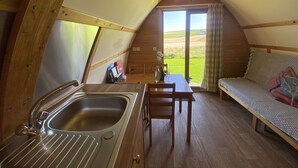 A cozy, triangular room with a wooden interior, a sink, a table with chairs, and a bed with a view of the countryside. - Secluded Cabin on the Banffshire Coast (Crovie)