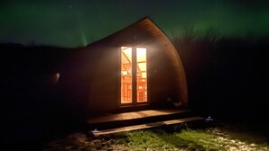 A small, dark wooden cabin with a single illuminated window, surrounded by a grassy area. - Secluded Cabin on the Banffshire Coast (Crovie)