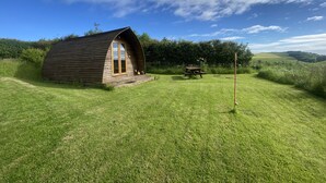 A wooden cabin with a pitched roof and large windows, situated in a grassy field with a picnic table and a bird feeder nearby. - Secluded Cabin on the Banffshire Coast (Crovie)
