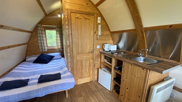 A compact, wooden cabin with a kitchenette, a bed with striped bedding, and a window with curtains. - Secluded Cabin on the Banffshire Coast (Crovie)