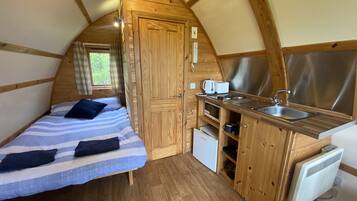 A compact, wooden cabin with a kitchenette, a bed with striped bedding, and a window with curtains.