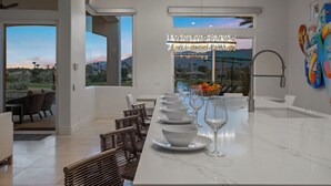A modern kitchen with a marble countertop, a dining area with chairs, and a view of the outdoors. - Desert Flower - Contemporary villa at PGA West (La Quinta)