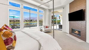 A spacious bedroom with a large bed, a fireplace, and a TV mounted on the wall. - Desert Flower - Contemporary villa at PGA West (La Quinta)