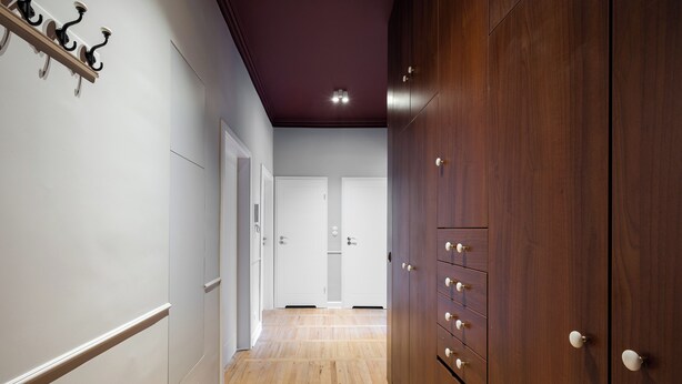 A hallway with wooden flooring, a dark ceiling, and a wooden wardrobe with multiple drawers. - Hala Mirowska Spacious Apartment (Warszawa)