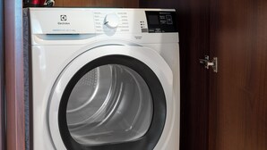 A front-loading washing machine with a digital control panel, a stainless steel door, and a wooden cabinet above it. - Hala Mirowska Spacious Apartment (Warszawa)
