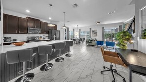 A modern kitchen with a large island, bar stools, and a dining area with a wooden table and chairs. - 1010 SS - Modern Comfort Oasis (Davenport)