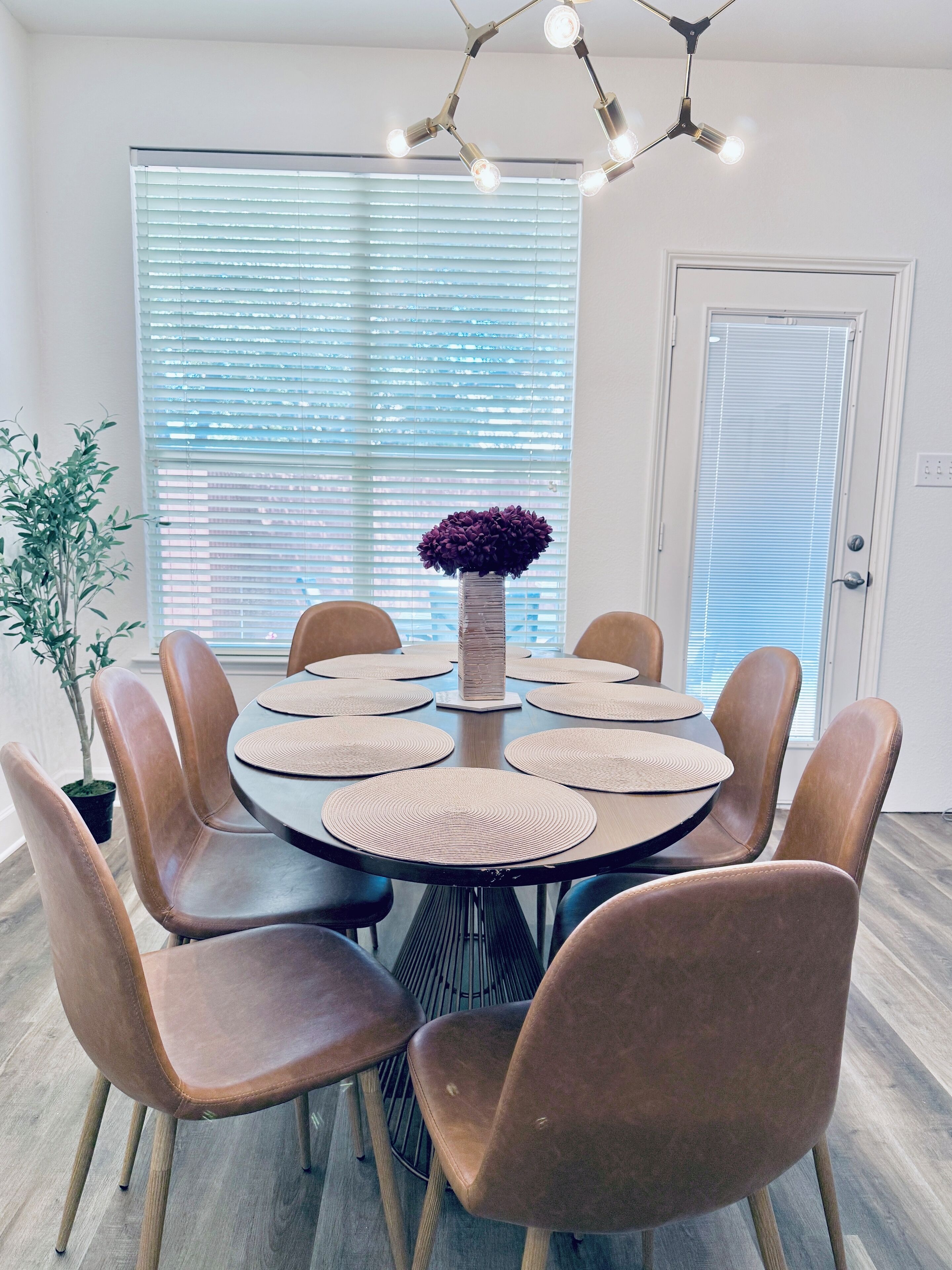 Un espace repas comprenant une table ronde, huit chaises et un vase central.