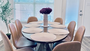 Un comedor con una mesa redonda, ocho sillas y un florero central.