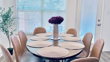 Un espace repas comprenant une table ronde, huit chaises et un vase central.