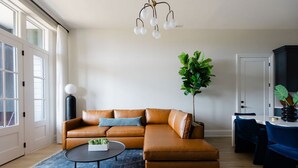 Uma sala de estar moderna com um sofá de couro em formato de L, uma mesa de centro redonda e uma planta grande.