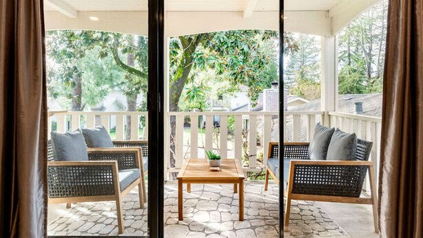 A covered outdoor seating area with wicker furniture and a central table, surrounded by a white railing and a stone-paved floor. - Serene 1 BR Condo at Silverado Resort (Napa)