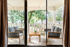 Un espacio de estar al aire libre con techo, amueblado con muebles de mimbre y una mesa central, rodeado por una barandilla blanca y un piso de piedra.