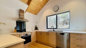 A modern kitchen with wooden cabinets, stainless steel appliances, a window with a view, and a clock on the wall. - Queenstown City •Walk to Town •Free Parking •A/C •Balcony •Mountain Views (Queenstown)