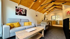 A modern living room with a grey sofa, yellow cushions, a wooden coffee table, and a kitchen area with a window. - Queenstown City •Walk to Town •Free Parking •A/C •Balcony •Mountain Views (Queenstown)